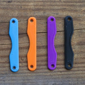 May include: Four plastic keychains in different colors: blue, orange, purple, and black. Each keychain has a small hole at the top.