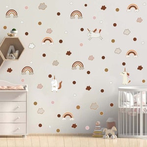 May include: A wall decorated with whimsical unicorn and rainbow wall decals in shades of brown, tan, and white. The decals include rainbows, clouds, and polka dots, creating a playful nursery theme.