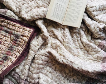 May include: A white and brown floral patterned quilt with a book lying on top. The quilt has a border of green and purple stripes. The book is open to a page with text.