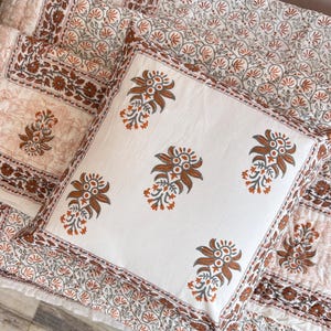 May include: A white cotton pillow cover with a brown floral pattern. The pillow cover has a border of smaller floral designs.
