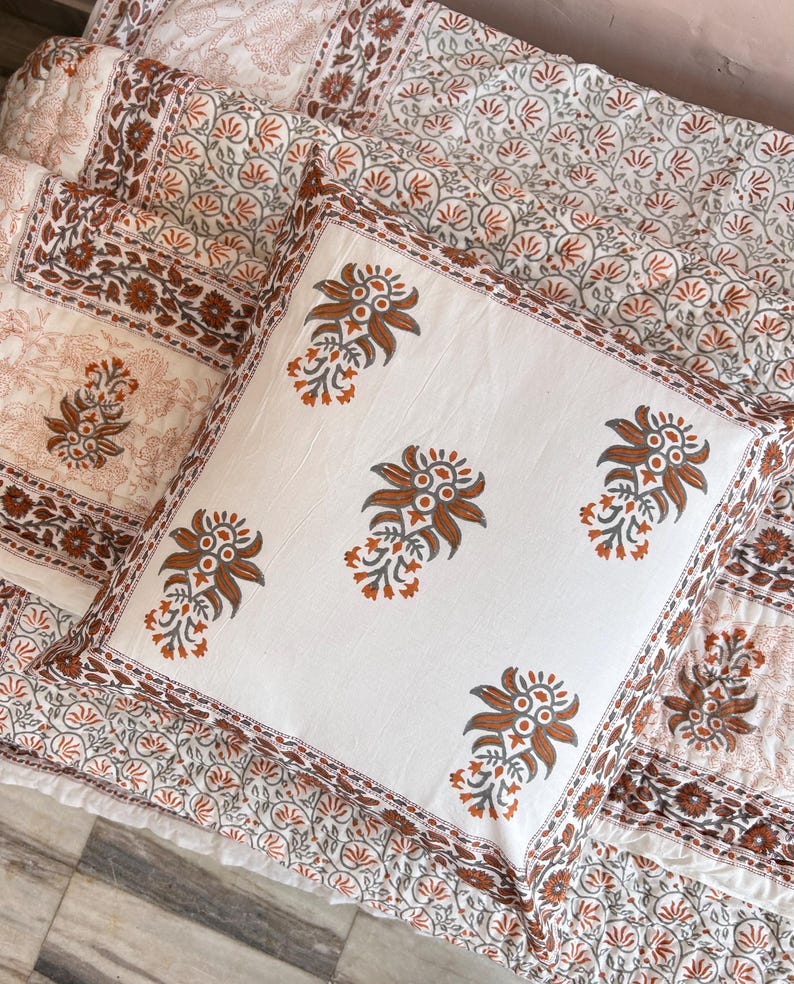 May include: A white cotton pillow cover with a brown floral pattern. The pillow cover has a border of smaller floral designs.