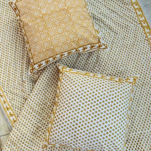 Può includere: Due cuscini quadrati con motivi bianchi e dorati poggiano su una coperta abbinata con motivi bianchi e dorati. Un cuscino presenta un motivo floreale, mentre l'altro ha un motivo a pois. I bordi dei cuscini e della coperta sono rifiniti con un bordo dorato.