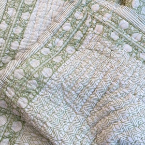 Pode incluir: Uma colcha de algodão branca e verde com um padrão geométrico. A colcha está dobrada ao meio e tem uma borda de desenhos florais.