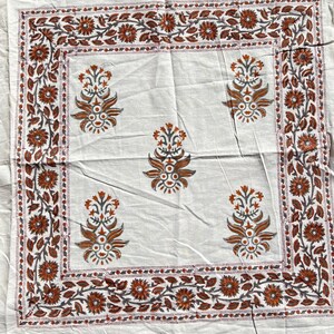 May include: White cotton tablecloth with a brown and gray floral print. The tablecloth has a border of flowers and leaves.