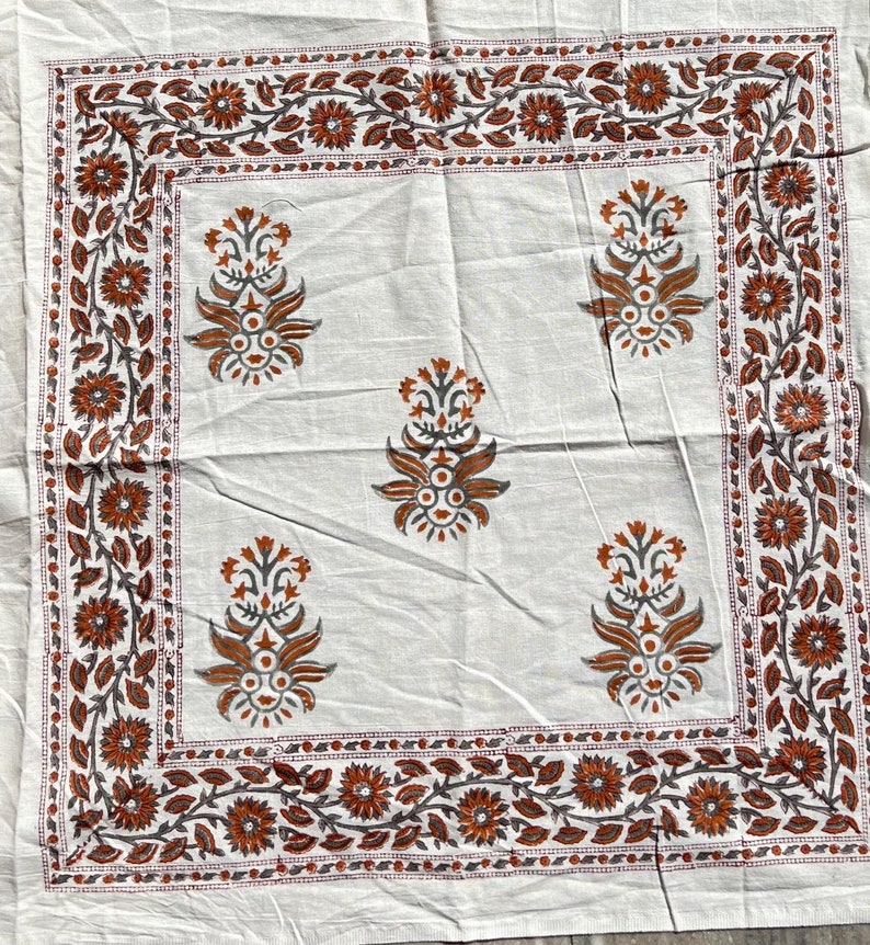 May include: White cotton tablecloth with a brown and gray floral print. The tablecloth has a border of flowers and leaves.