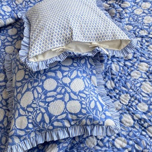 Könnte beinhalten: Eine blau-weiß geblümte Steppdecke mit zwei passenden Kissenbezügen. Ein Kissenbezug hat ein Rautenmuster, der andere ein Blumenmuster. Beide Kissenbezüge haben Rüschenkanten mit einem Streifenmuster.