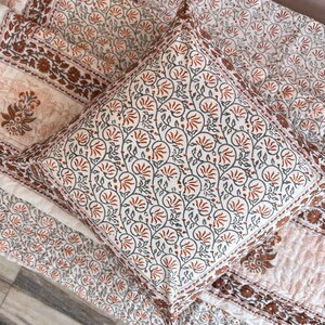 May include: A white and orange floral patterned pillow with a white background and orange and gray floral designs. The pillow is on top of a white and orange floral patterned quilt.