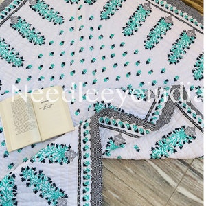 May include: White cotton quilt with a black and teal floral print. The quilt has a border with a black and white geometric pattern. The quilt is folded in half and a book is lying on top of it.