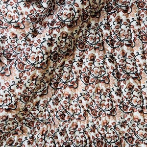 May include: A white cotton quilt with a brown and black floral pattern. The quilt is quilted in a diamond pattern.