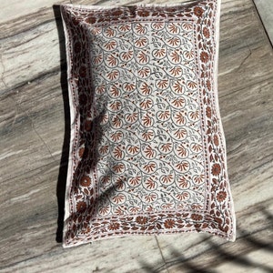 May include: A white pillowcase with a brown and gray floral pattern. The pillowcase has a border of brown and gray flowers.
