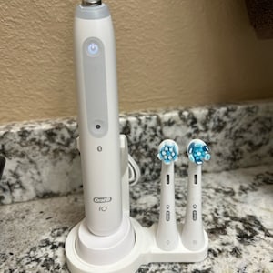 May include: A white electric toothbrush with a charging base and three replacement brush heads. The toothbrush has a blue light on the front and the text "Oral-B iO" on the side.