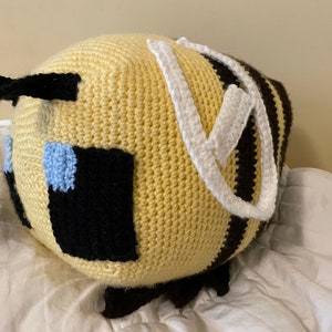 May include: A crocheted bee plush toy with black and brown stripes, yellow body, white wings, and blue eyes.