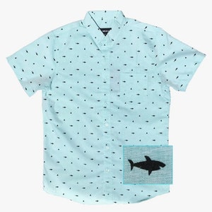 May include: A light blue short-sleeved button-down shirt with a white shark pattern. The shirt has a pocket on the left side and a single button closure. The shirt is made of a soft, comfortable fabric.