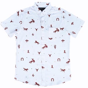 May include: White button-down shirt featuring a brown cowboy-themed pattern. The design includes horses, cowboys, boots, cacti, and other western motifs. The shirt has short sleeves and a chest pocket.