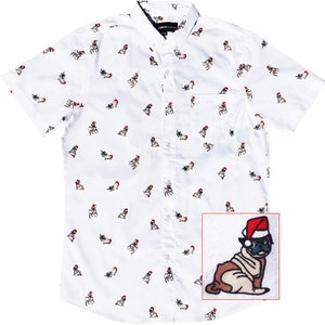 Puede incluir: Camisa blanca de manga corta con botones y un patrón repetido de carlinos con gorros de Papá Noel. La camisa tiene un solo bolsillo en el pecho.