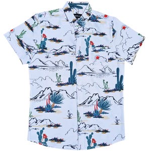 May include: White short-sleeve button-down shirt with a desert landscape print. The design features cacti, mountains, and red suns. The shirt has a classic collar and a single chest pocket.