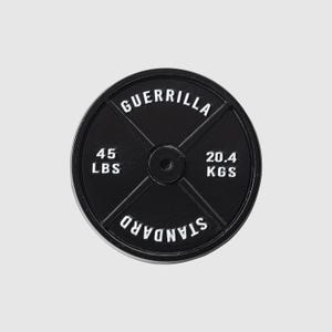 May include: A black weight plate with white lettering. The text reads "GUERRILLA", "45 LBS", "20.4 KGS", and "STANDARD". The weight plate is round with a central hole for the barbell.