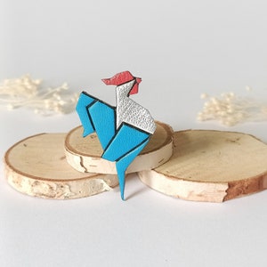 May include: A blue, white, and red origami rooster brooch. The rooster is made of leather and has a detailed design.