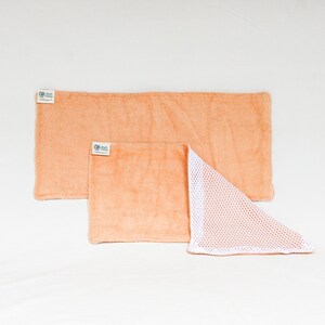 May include: Two peach-colored kitchen cloths with a white mesh backing. The cloths are made of a soft, absorbent material and are perfect for cleaning up spills and messes.