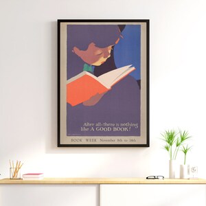 May include: A vintage poster advertising Book Week, featuring a child reading a book. The poster is in a black frame and has a purple, blue, and orange color scheme. The text on the poster reads "After all-there is nothing like A GOOD BOOK! BOOK WEEK November 8th to 14th."