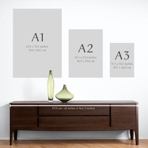 May include: Three different sizes of paper, labeled A1, A2, and A3, with their dimensions in inches and centimeters. The paper is displayed on a white wall above a dark brown wooden dresser with three drawers. The dresser is 62 inches long.