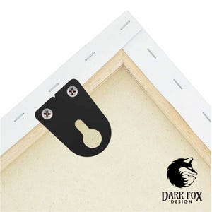 Può includere: Primo piano del retro di una stampa su tela, che mostra un gancio a dente di sega in metallo nero fissato con viti. La tela è tesa su un telaio di legno, con un bordo bianco graffettato al legno. Il logo Dark Fox Design è visibile.