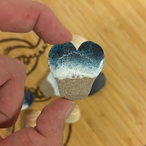 May include: A heart-shaped resin ornament with a blue and white ocean wave design and a brown sand bottom.