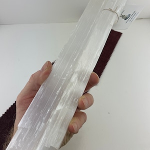 Può includere: Un fascio di bastoncini di selenite bianca, legati insieme con uno spago. I bastoncini sono lisci e hanno una texture naturale striata.