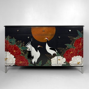 May include: A black sideboard cabinet featuring a gold moon design, cranes, and floral artwork. The cabinet has four drawers and two doors with silver handles. Red and white peonies and green leaves are also featured.