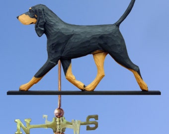 May include: A wooden black and tan walking dog weathervane. The dog is carved in a realistic style and is mounted on a black metal rod with a copper ball finial. The weathervane also includes a compass rose with the letters N, S, E, and W.