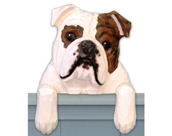 May include: A white and brown bulldog figurine peeking over a blue fence. The bulldog has a white face with brown ears and a brown patch on its eye.