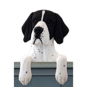 May include: A black and white English Pointer dog figurine peeking over a blue surface. The dog has black ears and a white body with black spots. The figurine is made of wood and has a realistic appearance.
