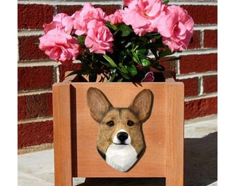 May include: A wooden planter box with a brown and white corgi dog face painted on the front. The planter is filled with pink flowers.