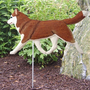 May include: A wooden figurine of a brown and white Siberian Husky dog running. The figurine is mounted on a metal stake for outdoor display.