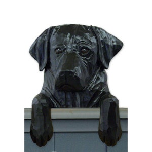 May include: A black Labrador Retriever dog figurine peeking over a ledge. The figurine is carved from wood and painted black.