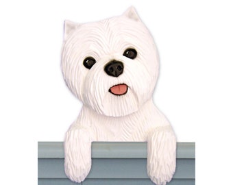 May include: A white West Highland White Terrier figurine peeking over a blue fence. The figurine is made of painted resin and has a realistic appearance.