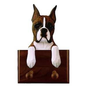 May include: A wooden wall hook featuring a carved boxer dog with brown and white fur. The dog is peeking over the top of the hook, which has two wooden knobs for hanging items.