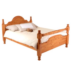 May include: A wooden bed frame with a warm, honey-toned finish featuring a high, arched headboard and a matching footboard. The bed is dressed with a plain white duvet cover, two light beige pillows, and two small, round, textured decorative spheres.