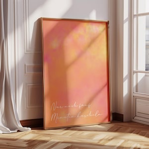 Op de afbeelding: Een ingelijste kunstdruk met een verloop van oranje, gele en roze tinten. Het kunstwerk bevat de tekst "Nur noch fünf Minuten kuscheln" in een sierlijk handschrift. De lijst is goudkleurig en de print leunt tegen een witte muur.
