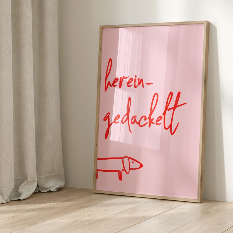 Pode incluir: Uma impress&atilde;o emoldurada rosa com o texto "herein-gedackelt" em escrita cursiva vermelha. Uma ilustra&ccedil;&atilde;o de dachshund vermelha est&aacute; na parte inferior da impress&atilde;o.