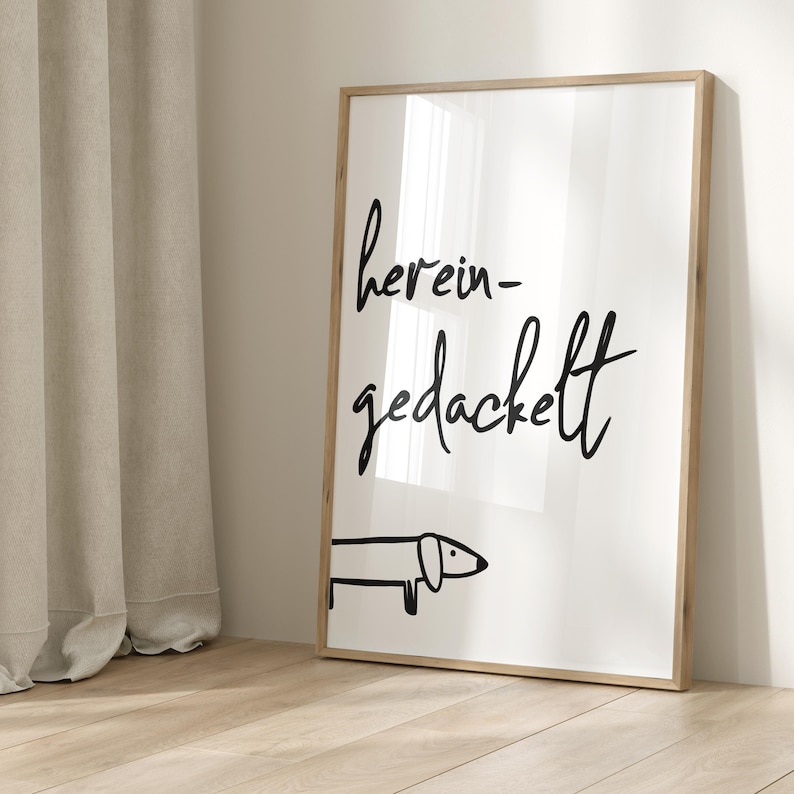 Pode incluir: Uma impress&atilde;o em preto e branco com o texto "herein-gedackelt" em uma fonte cursiva. Uma simples ilustra&ccedil;&atilde;o de dachshund preto est&aacute; abaixo do texto.