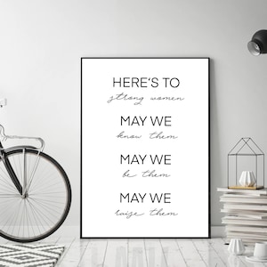 Könnte beinhalten: Ein schwarz gerahmter Druck mit dem Text "HERE'S TO strong women. MAY WE know them. MAY WE be them. MAY WE raise them." Der Druck wird in einem modernen Innenraum vor einer weißen Wand präsentiert.