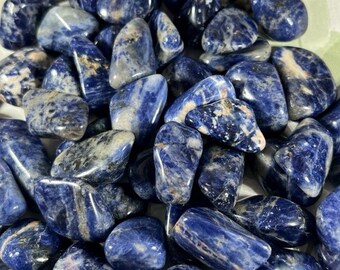 May include: A collection of tumbled blue and white sodalite stones. The stones are smooth and polished, with a variety of patterns and swirls.