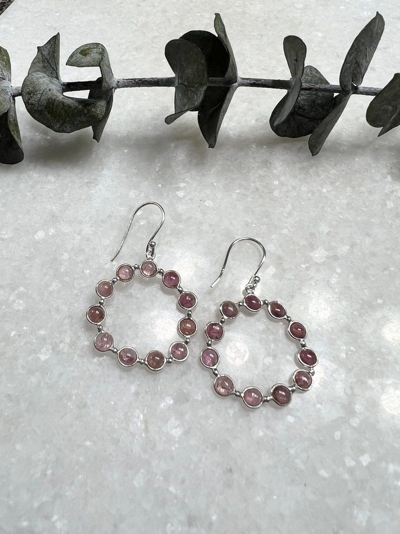 Puede incluir: Un par de pendientes de aro de plata con detalles de piedras preciosas rosas. Cada pendiente tiene un c&iacute;rculo de piedras rosas.