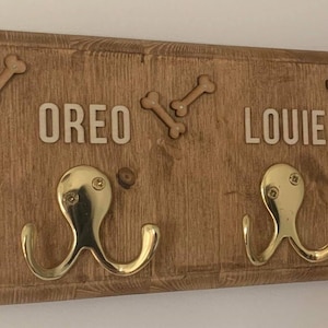 May include: Wooden dog lead rack with two brass hooks. The rack has the names "OREO" and "LOUIE" written on it, and three wooden bone shapes.