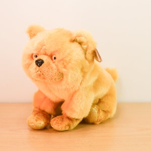 May include: A plush golden brown chow chow dog toy. The toy has a black nose and black eyes.
