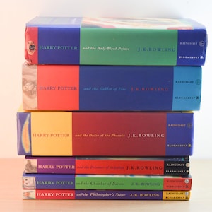 May include: A vertical stack of six hardcover Harry Potter books by J.K. Rowling, featuring colourful spines with titles including The Half-Blood Prince, Goblet of Fire, Order of the Phoenix, Prisoner of Azkaban, Chamber of Secrets, and Philosopher's Stone.