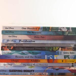 May include: A stack of ten colourful paperback books featuring Disney characters on the covers. The books are titled "One Hundred and One Dalmatians", "The Rescuers", "Peter Pan", "Pocahontas", "Bambi", "The Rescuers Down Under", "The Little Mermaid", "Beauty and the Beast", "Aladdin", "The Great Mouse Detective", and "Sleeping Beauty".