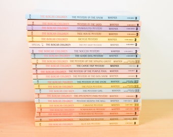 Puede incluir: Una pila de libros antiguos de "The Boxcar Children". Los lomos muestran títulos como "Misterio en la nieve" y "El misterio del fútbol". Los libros tienen cubiertas coloridas y están colocados sobre una superficie clara.