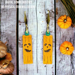 May include: A pair of dangle earrings featuring a pumpkin face design. The earrings are made of orange leather with a green and gold accent. The earrings are hanging from a wooden surface.